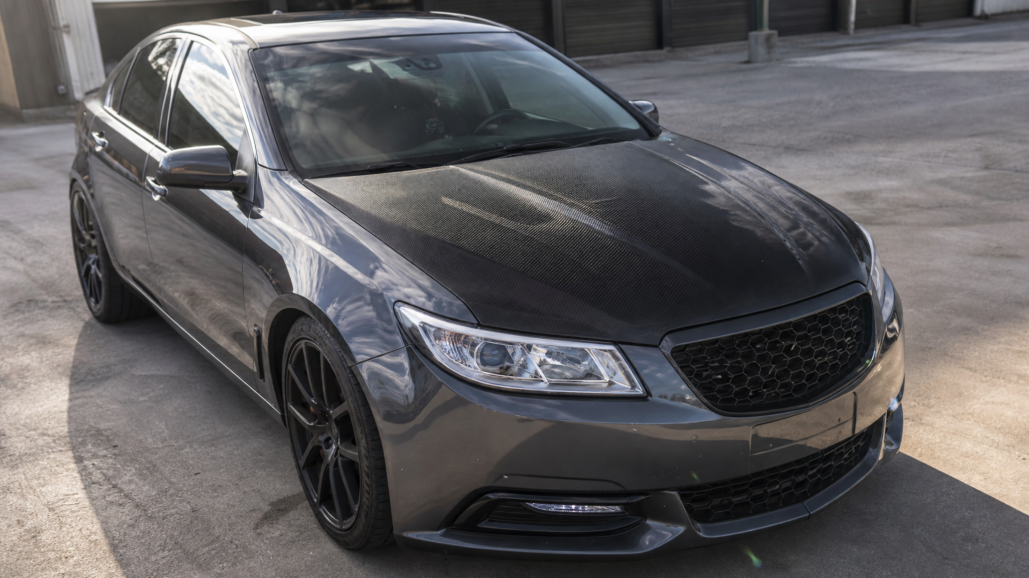 Daily-driver car with realistic black carbon fiber vinyl hood wrap in afternoon sunlight
