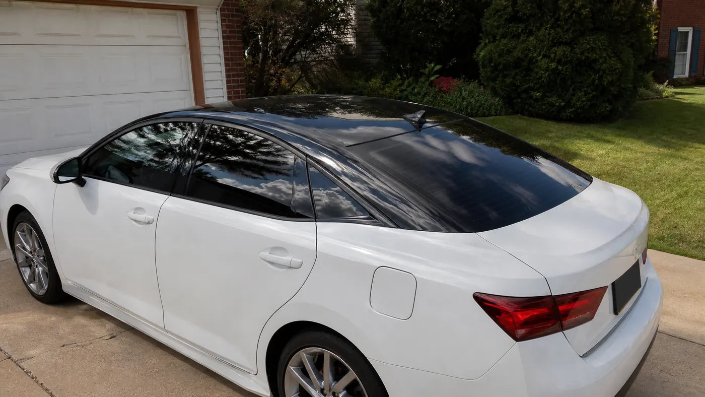 White car with gloss black roof vinyl wrap in natural driveway light with tree and sky reflections